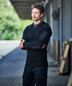 A man with his arms folded wearing a black NATO security jumper and black cargo trousers.