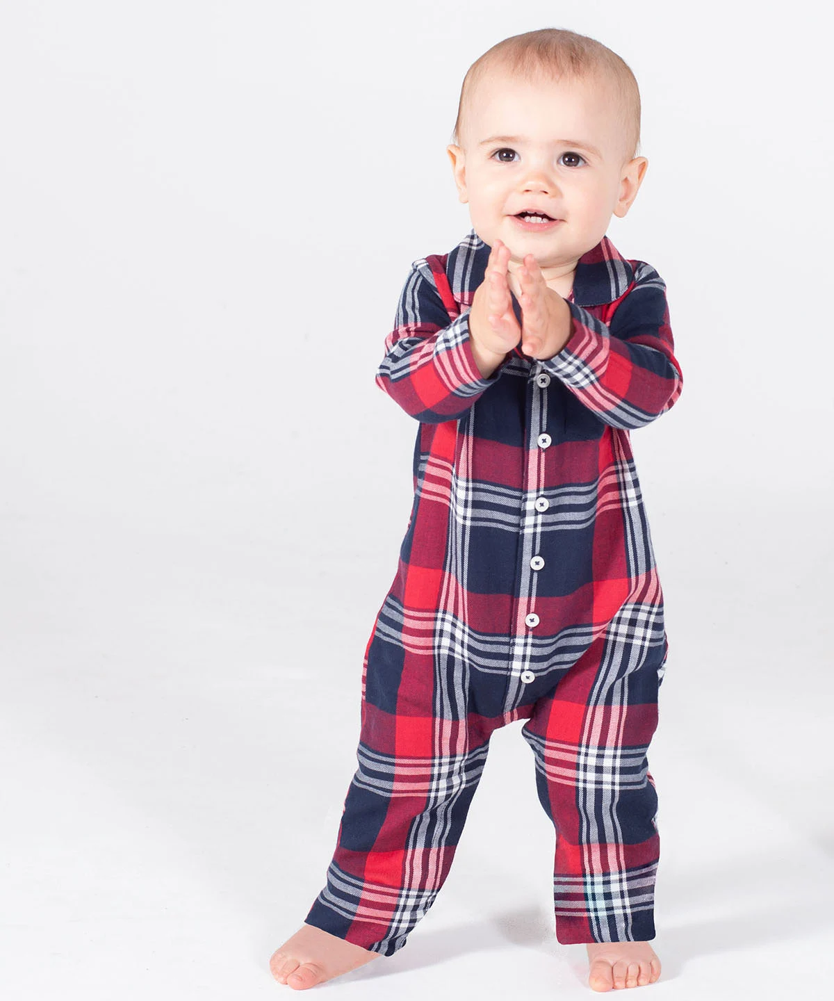 An infant with their hands together stood up wearing the tartan all-in-one