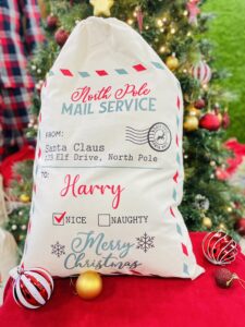 A natural coloured sack printed to the front. Text surrounded with a blue and red dashed line. Text Reads: North Pole / MAIL SERVICE / FROM: / Santa Claus / 123 Elf Drive, North Pole / TO: / [Name] / NICE NAUGHTY / Merry / Christmas