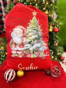 A red sack printed to the front with Father Christmas stood next to a Christmas tree. Above the image, in cursive black writing reads: "close your eyes sleep tight". Below the image, in black cursive writing reads: "Santa is on his way tonight!". Below the bottom black text, in cream cursive writing reads: "Sophie"