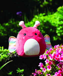 Frontal view fo the butterfly squidgy outside amongst vibrant green plants and pink flowers