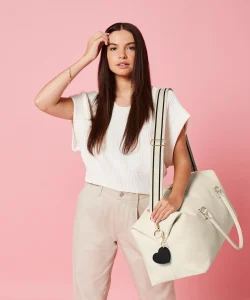 A woman with dark brown hair dressed in a white top and cream trousers with the cream-coloured oyster Iris weekender bag hung over her shoulder by its shoulder strap