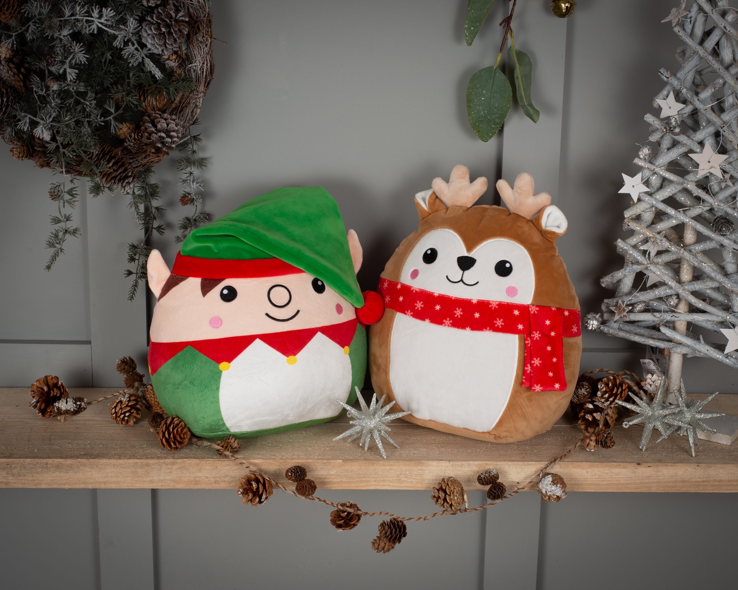 Frontal view of the personalised Christmas Elf and Reindeer Squidgy's surrounded by pine cones and Christmas ornaments against a grey wall