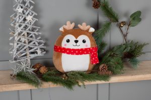 Frontal view of the Christmas reindeer Squidgy amongst pine cones and pine needles with a grey Christmas tree decoration to the left