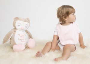 A large brown owl teddy next to a toddler wearing a pink bib. On the owls belly is sample personalised text that reads: "My name is Otto I belong to Luca". The text on the belly is light brwon and baby pink.