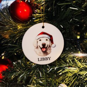 A photos of a personalised round ceramic christmas decoration with a watercolour image of a dog with it's name below