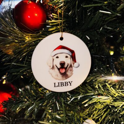 A photos of a personalised round ceramic christmas decoration with a watercolour image of a dog with it's name below