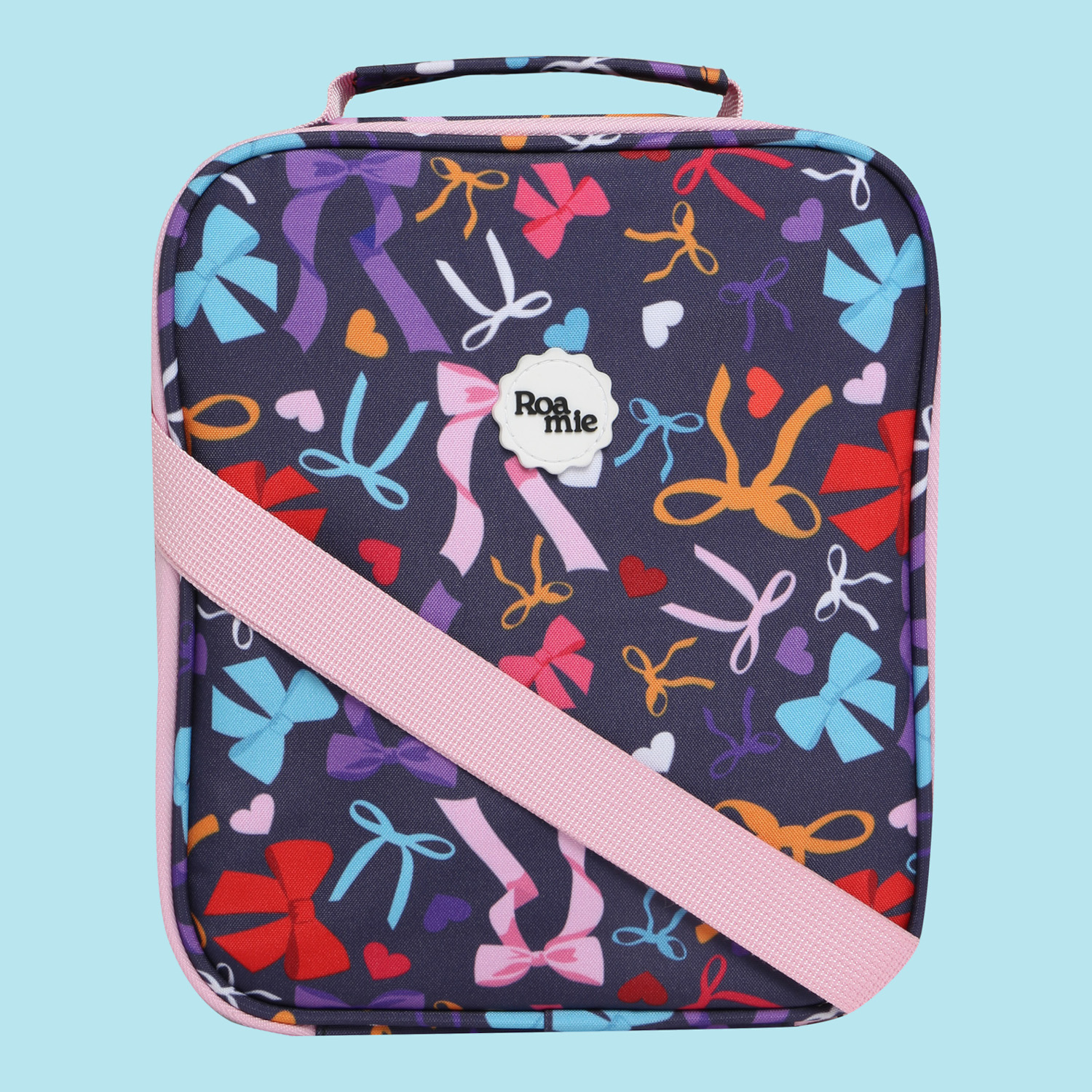 In front of a sky blue background: a navy lunch bag with imagery of bows of various shapes, sizes, and colours. Amongst the bows are love hearts of different colours.