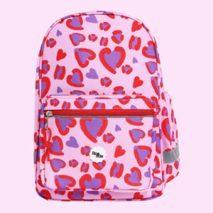 In front of a baby pink background: a baby pink backpack with imagery of varying sized child-like drawings of hearts with a disjointed red outline and purple center.